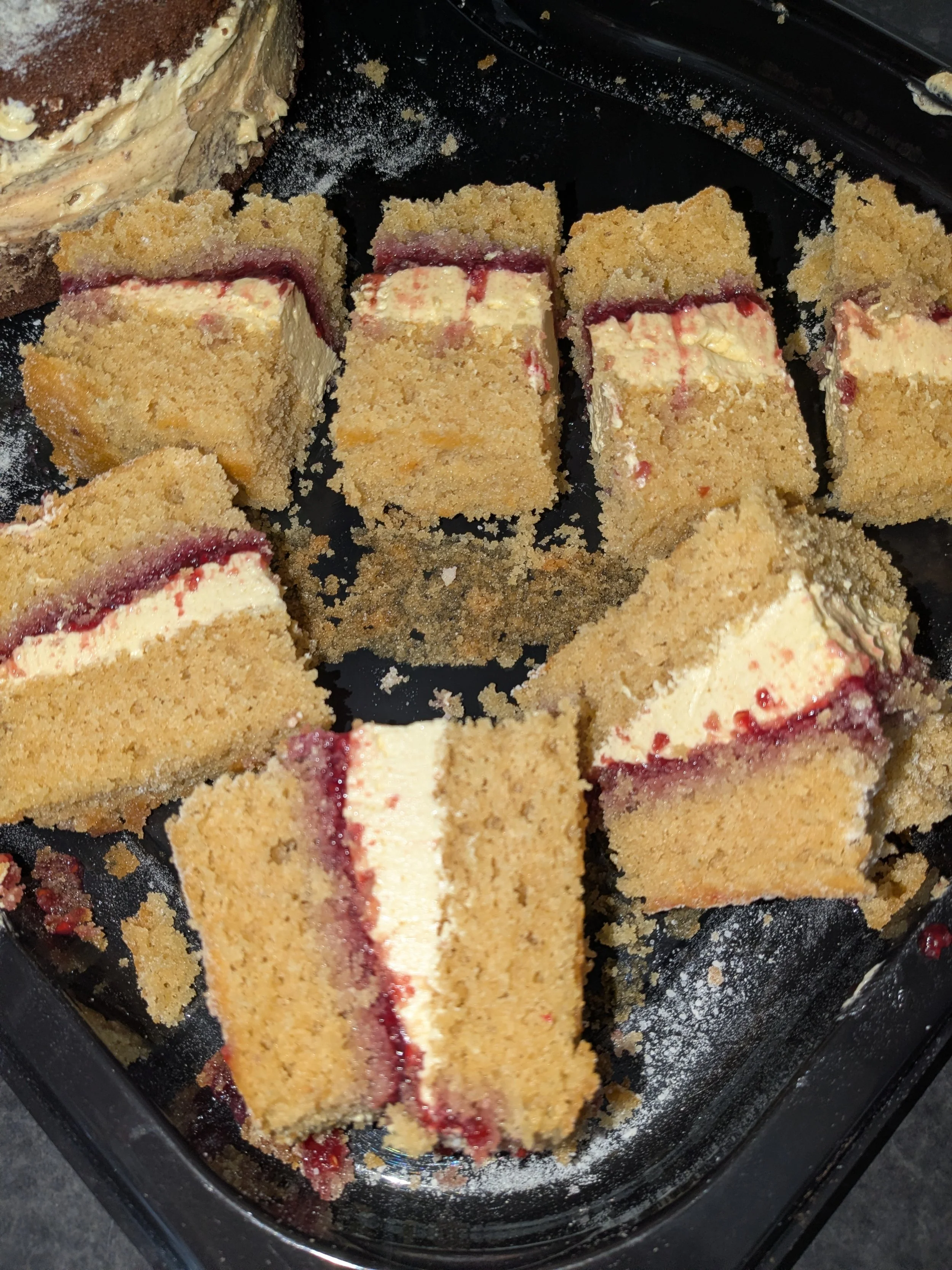 Slices of cheesecake with a graham cracker crust and a cherry or berry topping, inside a black plastic container.