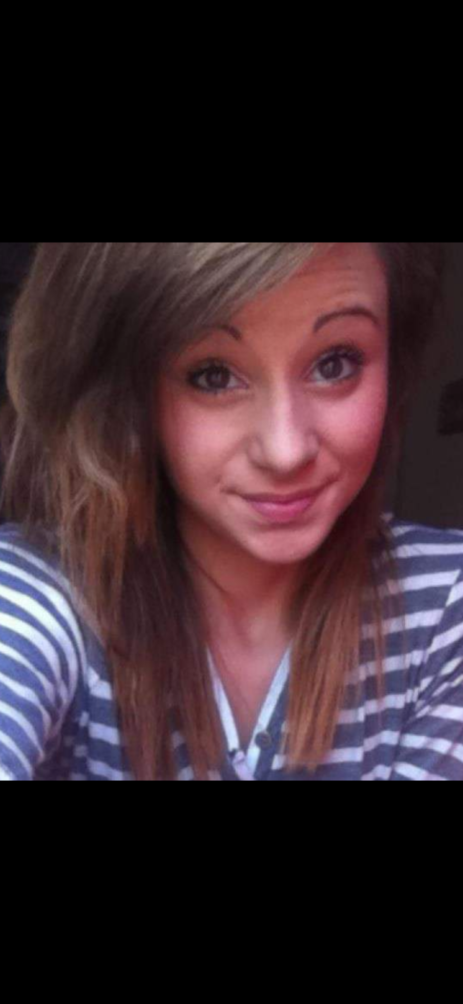 A young woman with long, light brown hair and blue eyes, smiling while taking a selfie. She is wearing a blue and white striped shirt.