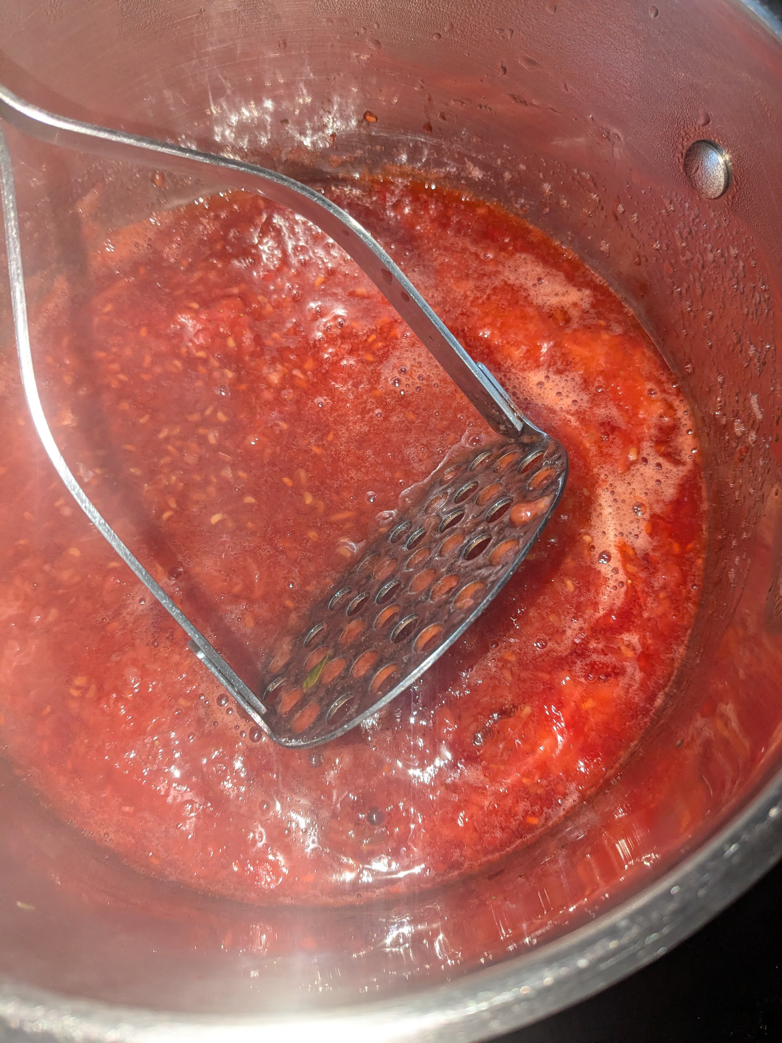 A saucepan with a red sauce and a slotted spoon inside it.