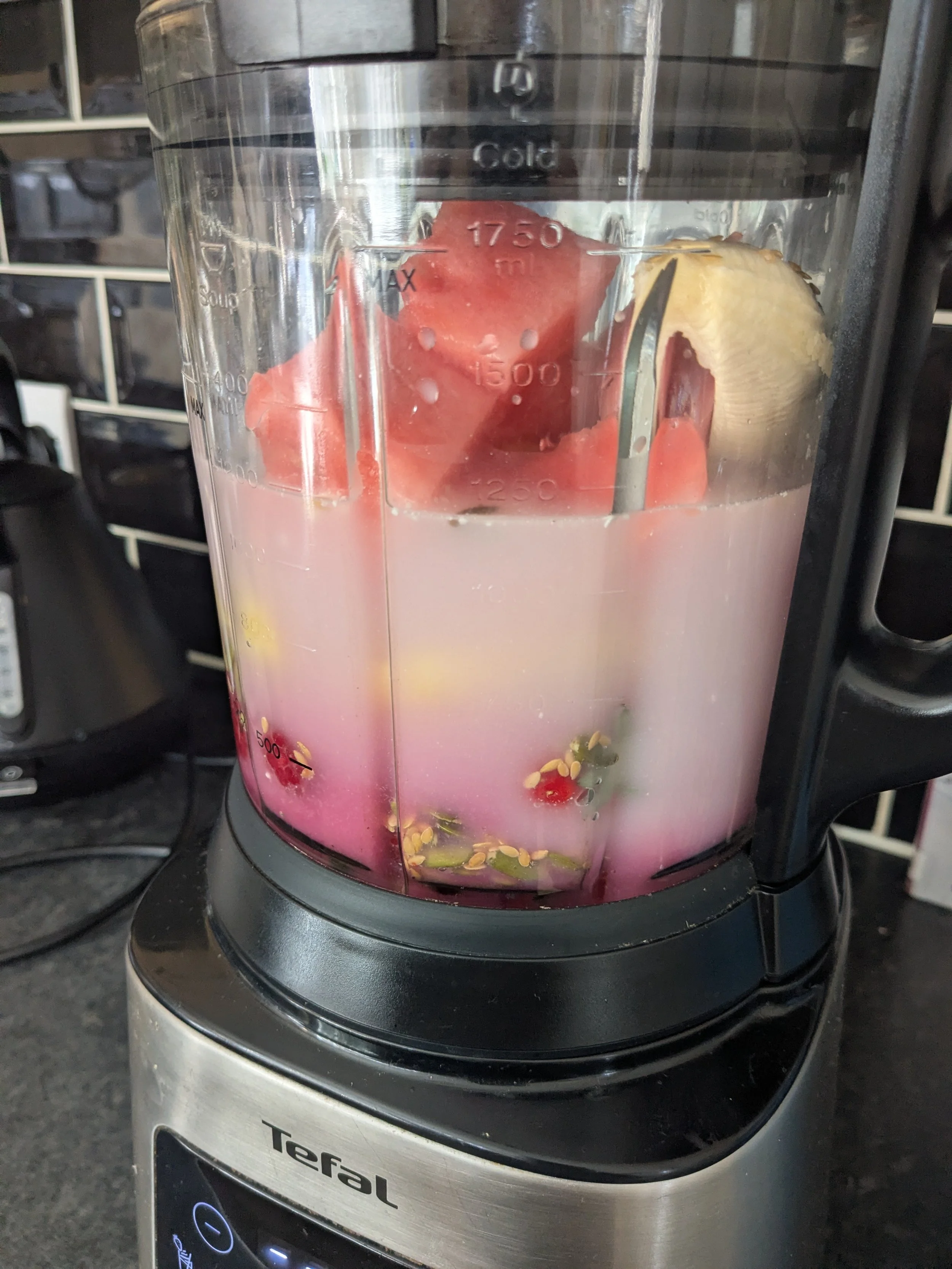 A blender with pink liquid inside, containing watermelon and banana, on a kitchen countertop.
