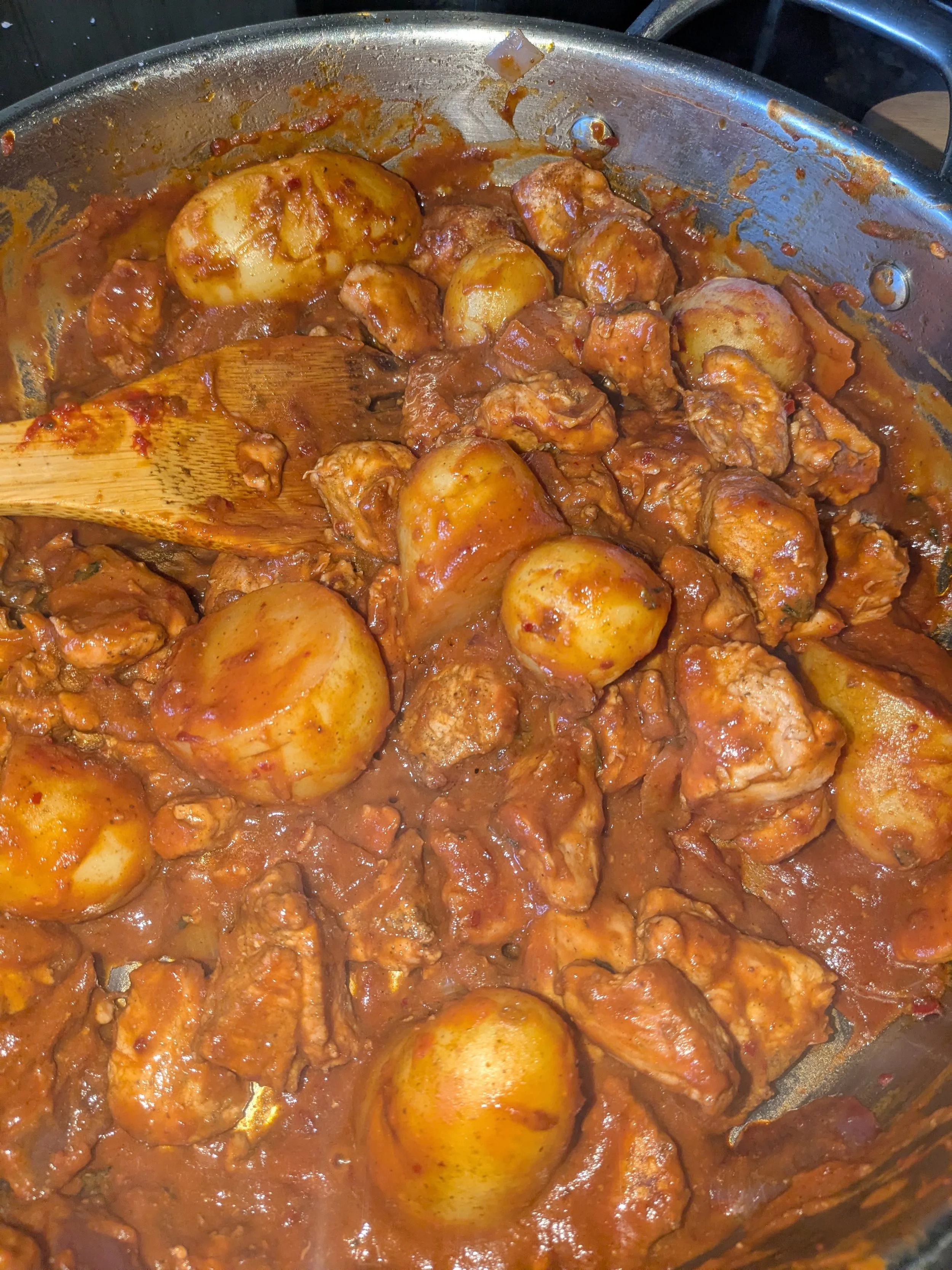 Potatoes and chicken cooking in a tomato-based sauce in a large skillet.