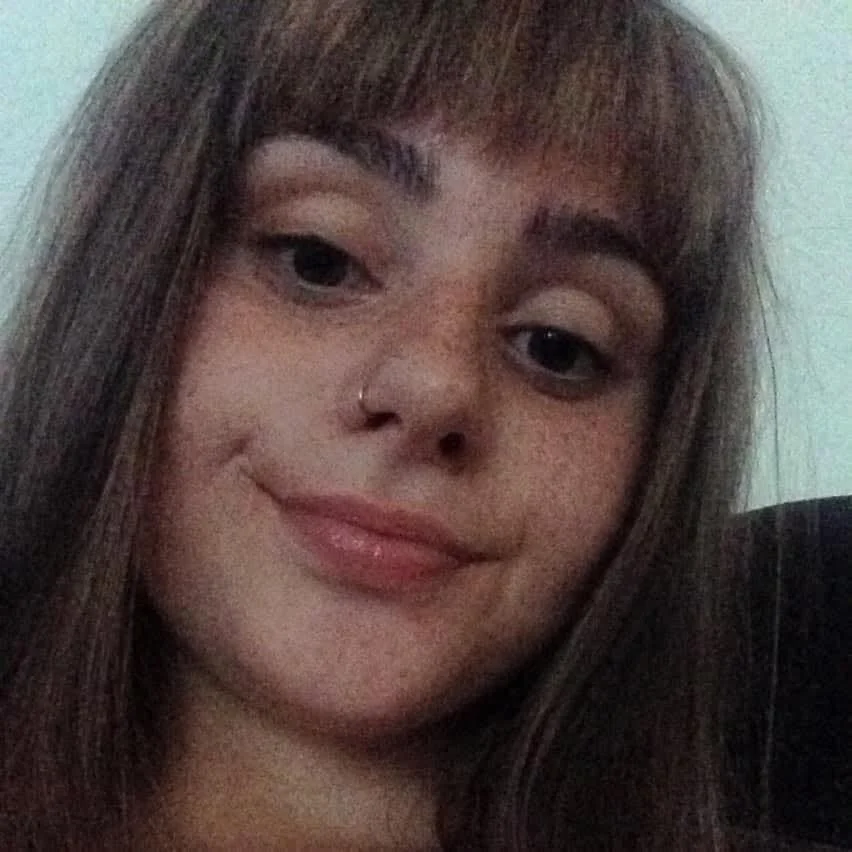 Close-up of a young woman with brown hair, long bangs, light skin, a nose ring, and a slight smile.