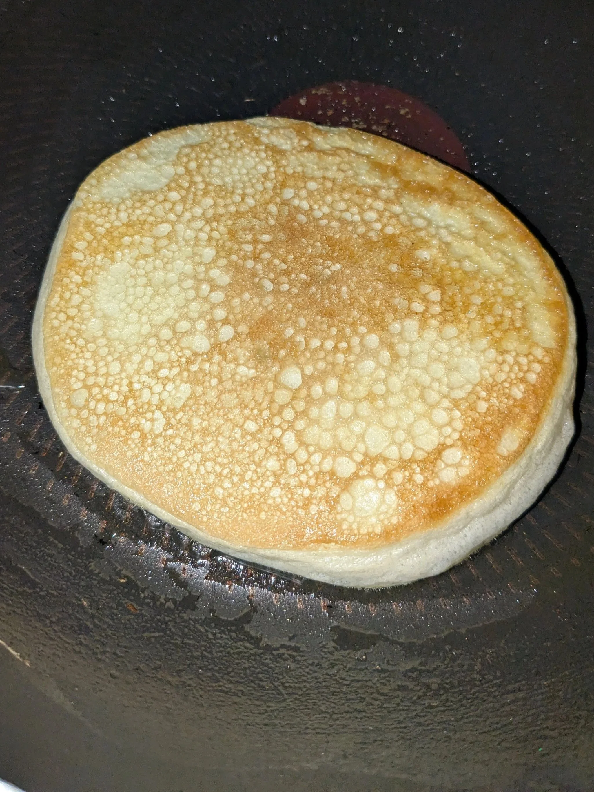 A pancake cooking in a black frying pan.