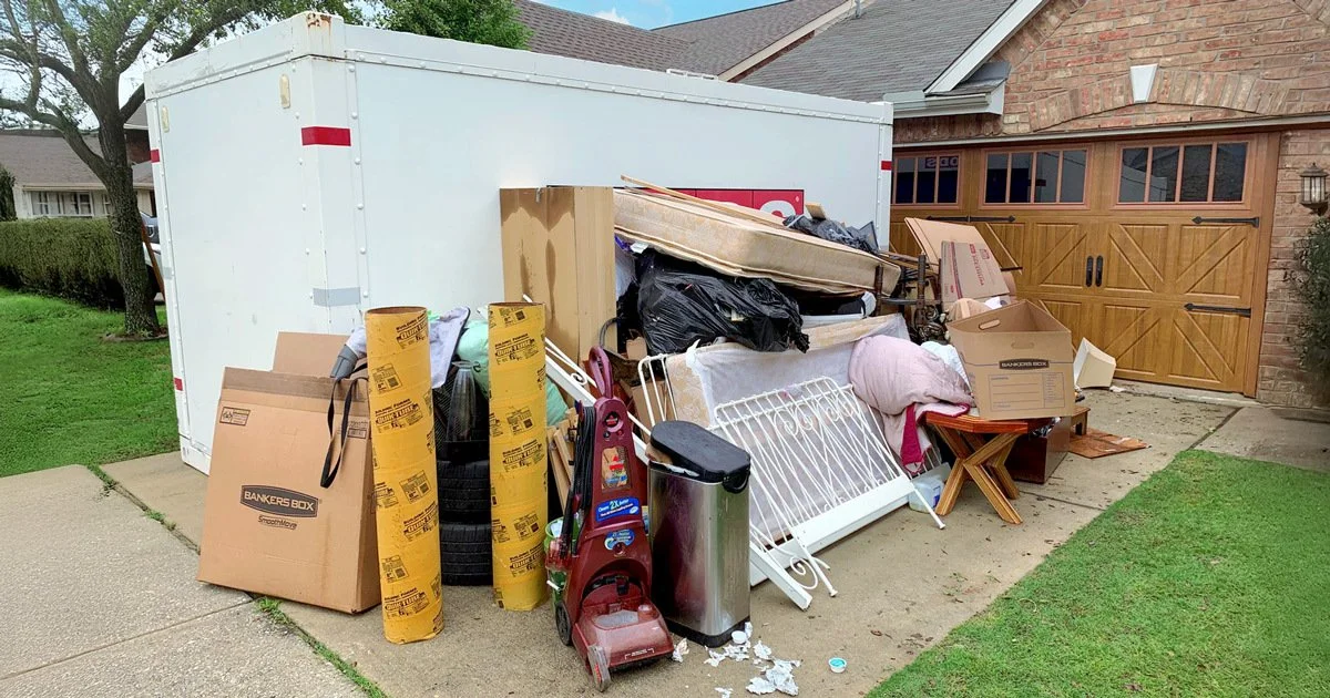 Overflowing trailer filled with various household items and boxes outside a house.
