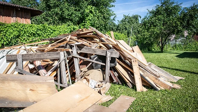 Piles of chopped and broken wood and debris in a backyard with grass and trees.