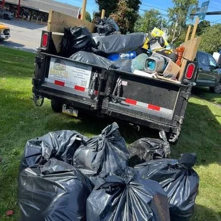 Pickup truck with open tailgate overflowing with trash bags; several trash bags on the ground nearby.