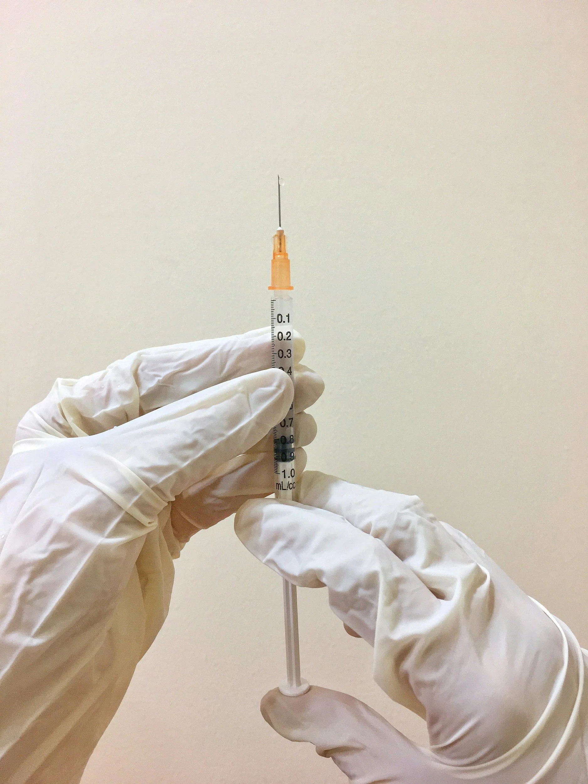 A gloved hand holding a syringe with a needle, ready for medical injection, against a plain background.