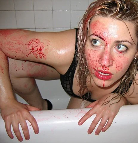 Woman with wet hair and blood on her face and arm, leaning over the edge of a bathtub.