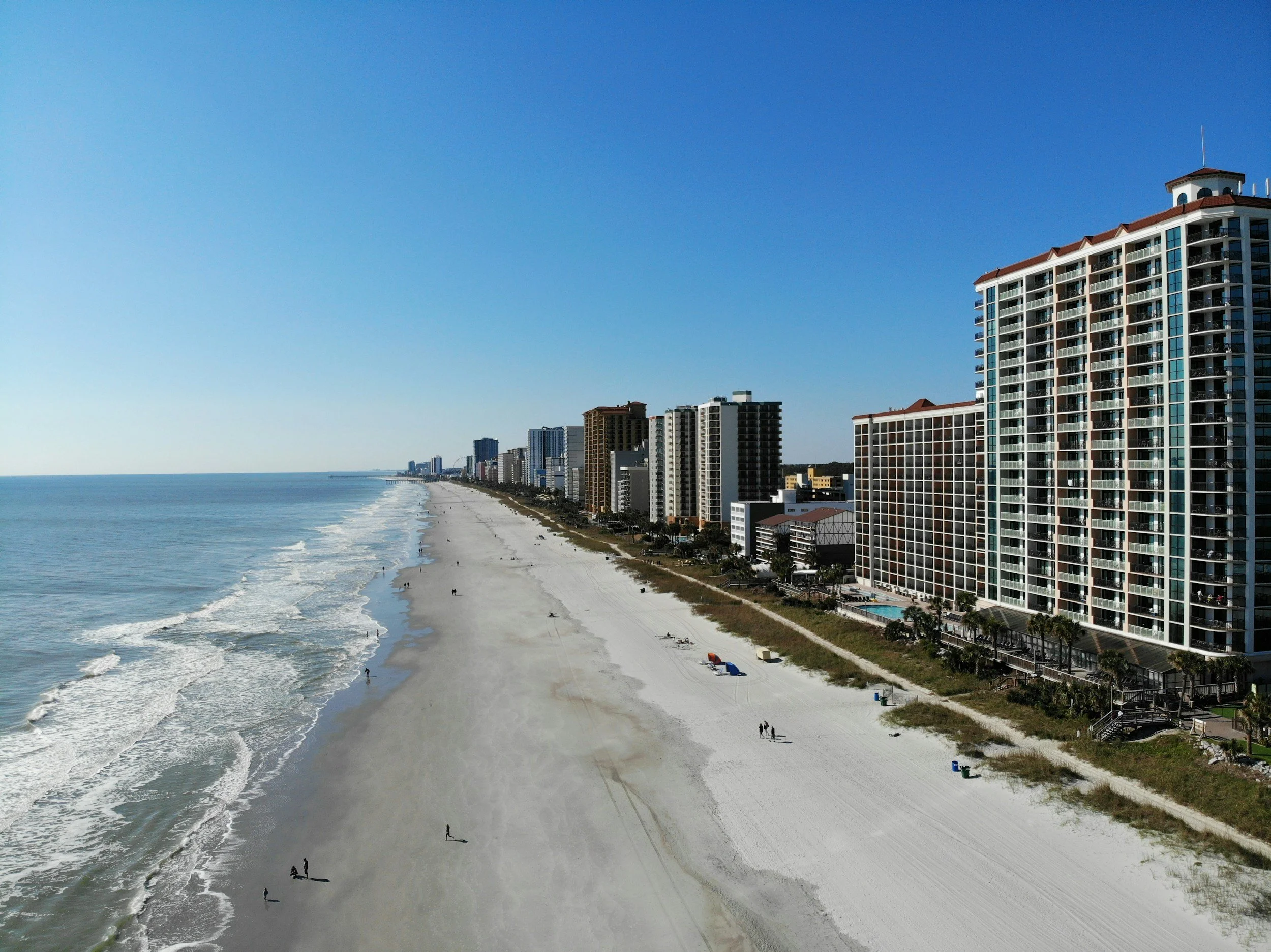 Aerial view of a seaside city with tall buildings along the coast, sandy beach, and ocean waves.