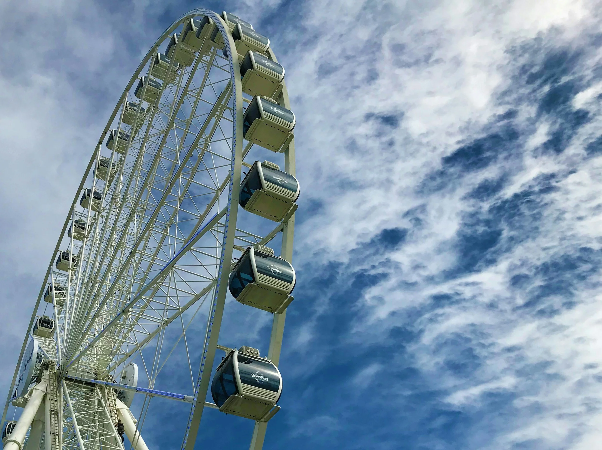A large Ferris wheel with enclosed gondolas marked 'SkyWheel' against a partly cloudy sky.