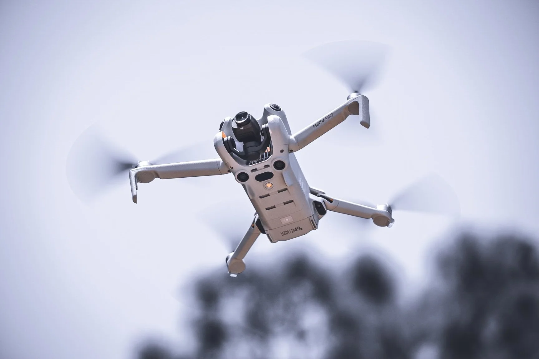 A quadcopter drone flying in the sky with blurred trees in the background.
