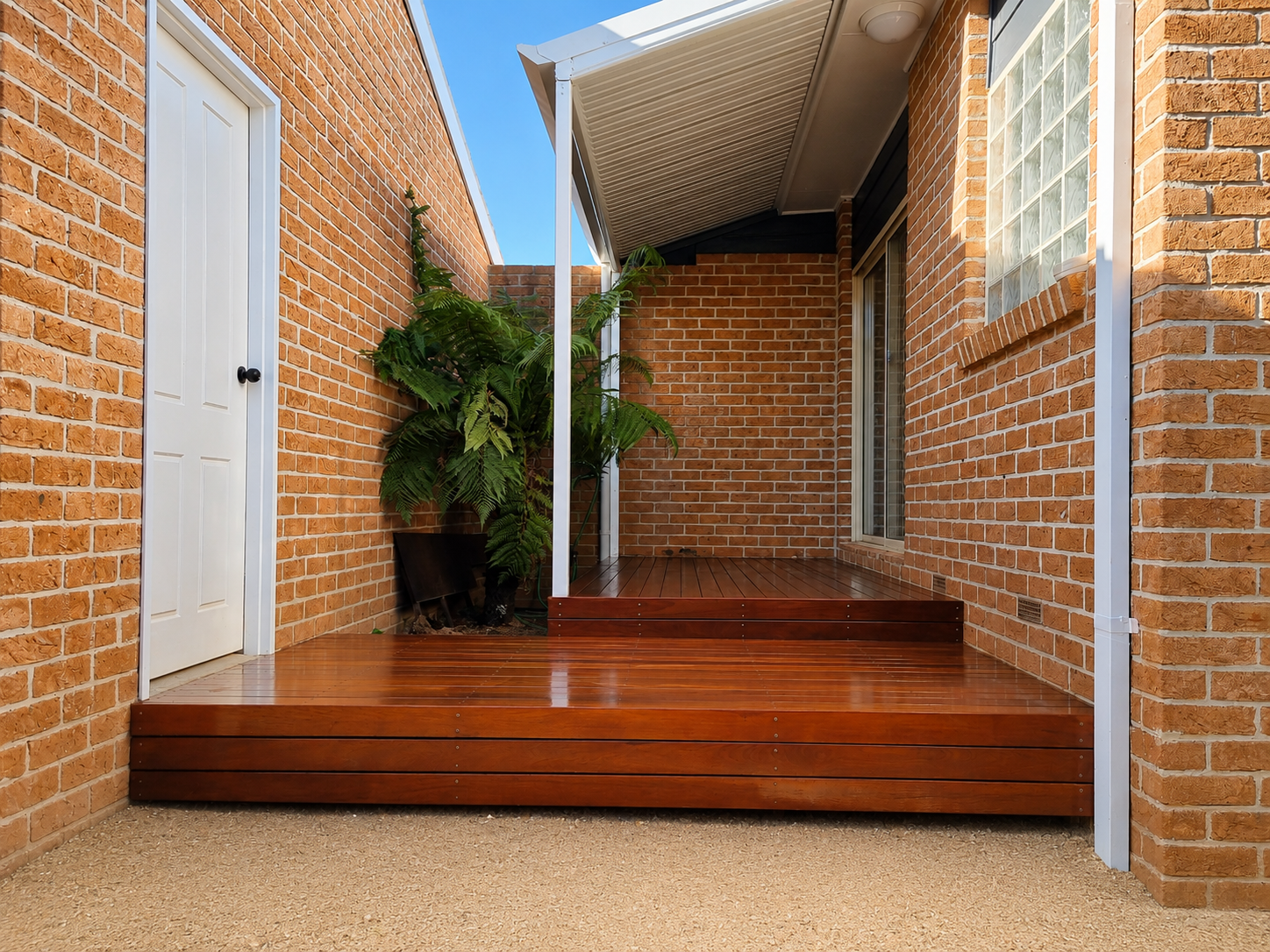 Back porch with wooden deck, brick walls, potted plants, and a glass sliding door.