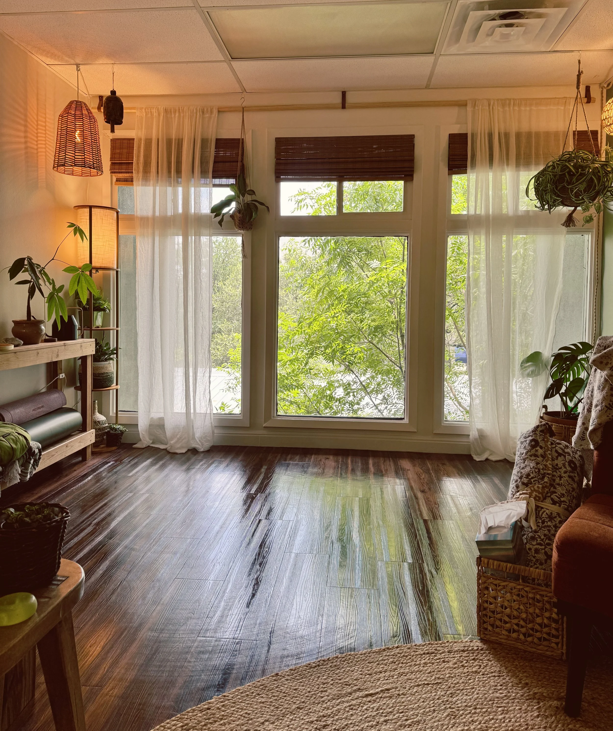 a large, open light-filled office with wood floors, large windows, plants, blankets, yoga mats, and lamps