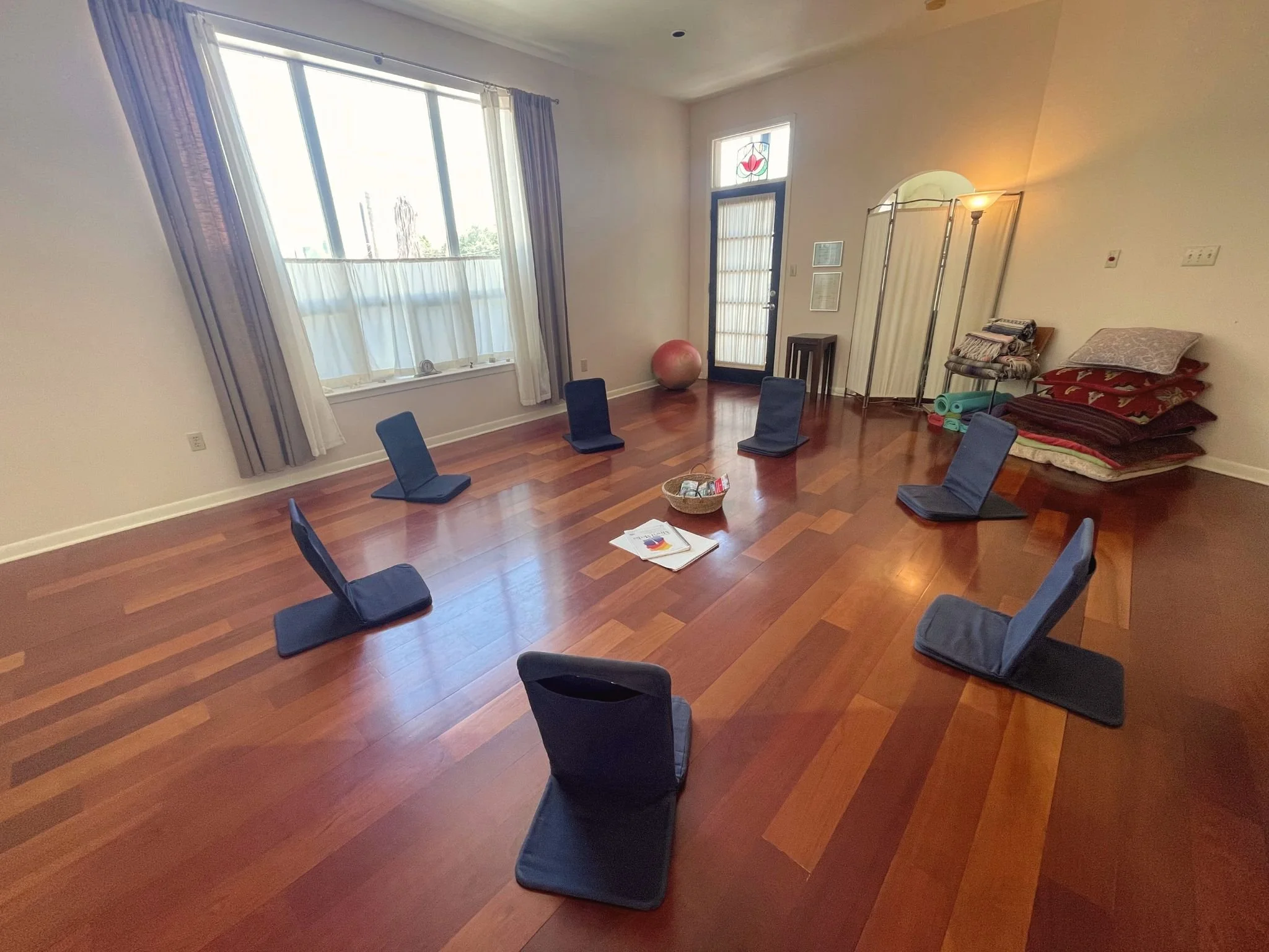 a circle of floor chairs on wood floors in a light-filled studio, with art supplies in the middle
