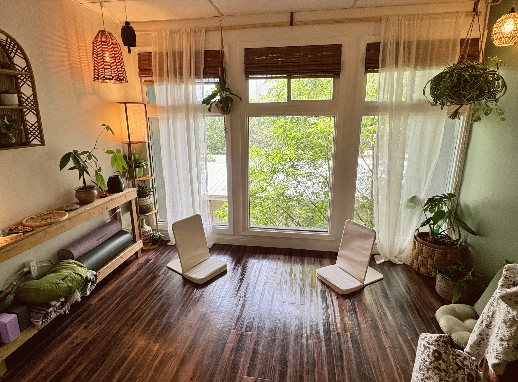 a light filled office with two floor chairs across from each other in front of large windows; next to plants, lamps, and yoga mats
