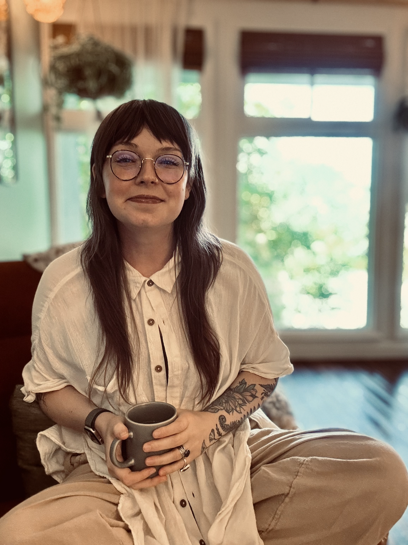 smiling therapist holding a cup of tea, sitting criss cross in a chair in a light-filled office