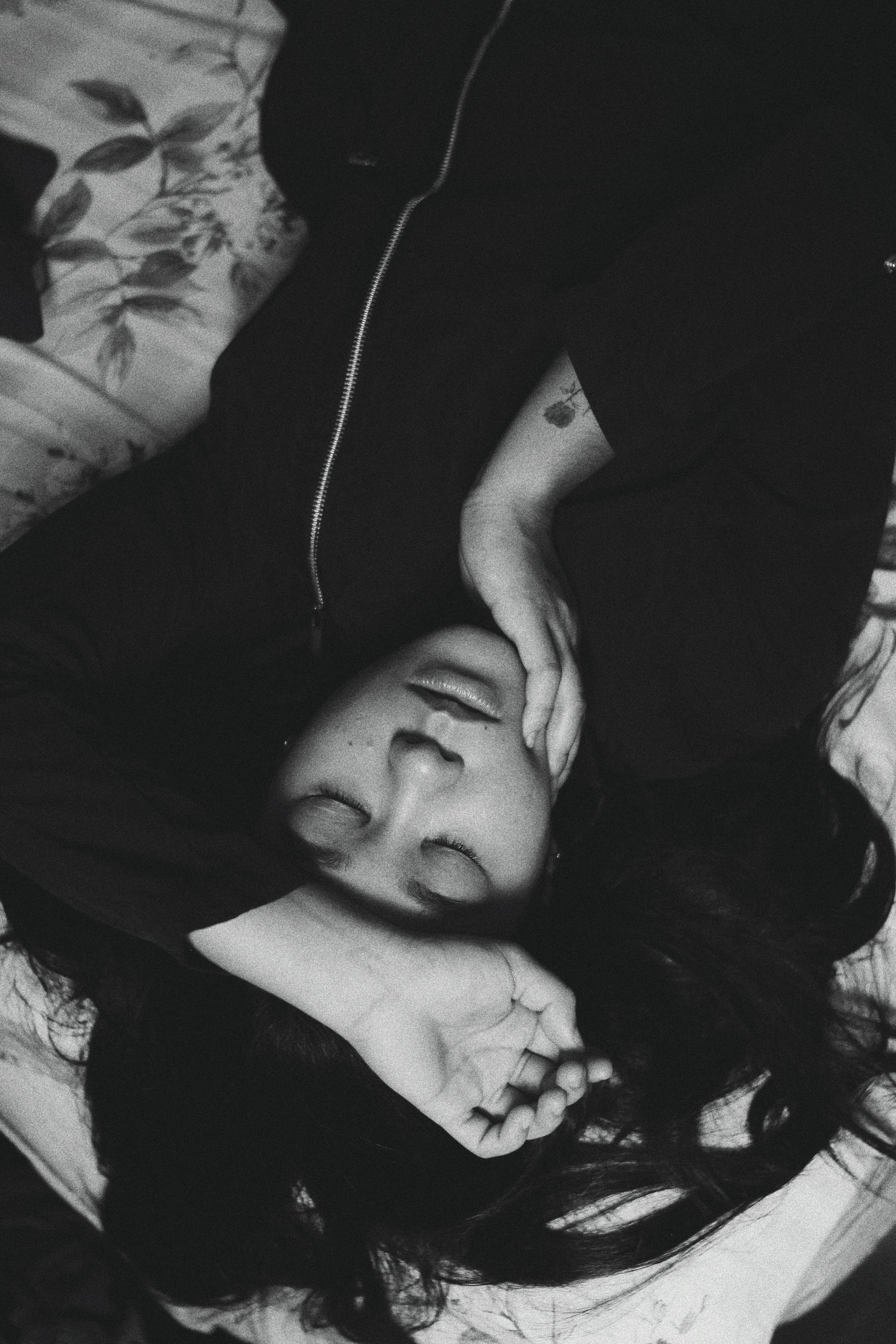 Black and white portrait of a woman lying down with eyes closed, hand near her face, evoking restlessness and emotional weight.