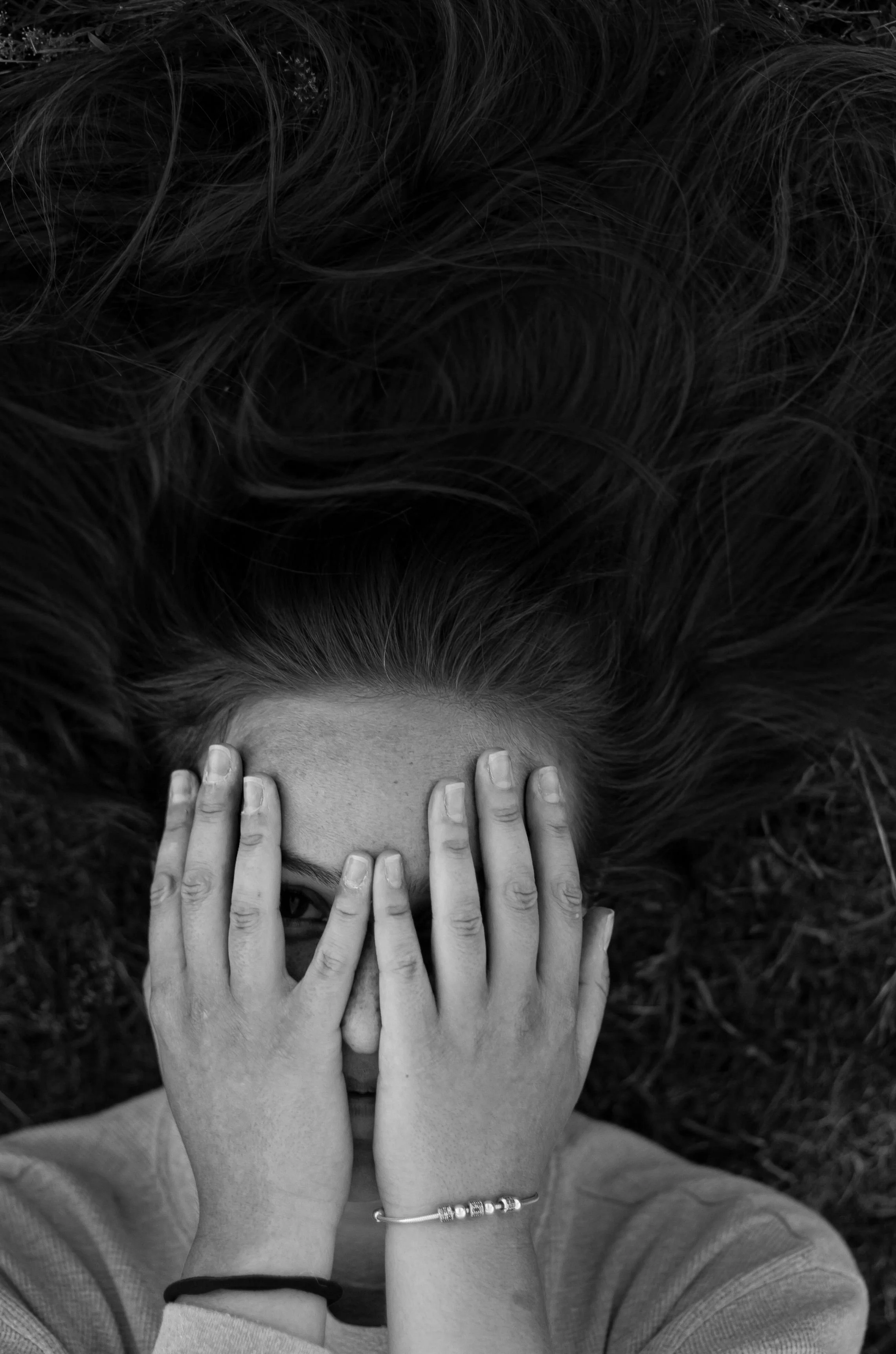 Black and white photo of a person covering their face with both hands, conveying overwhelm and distress.