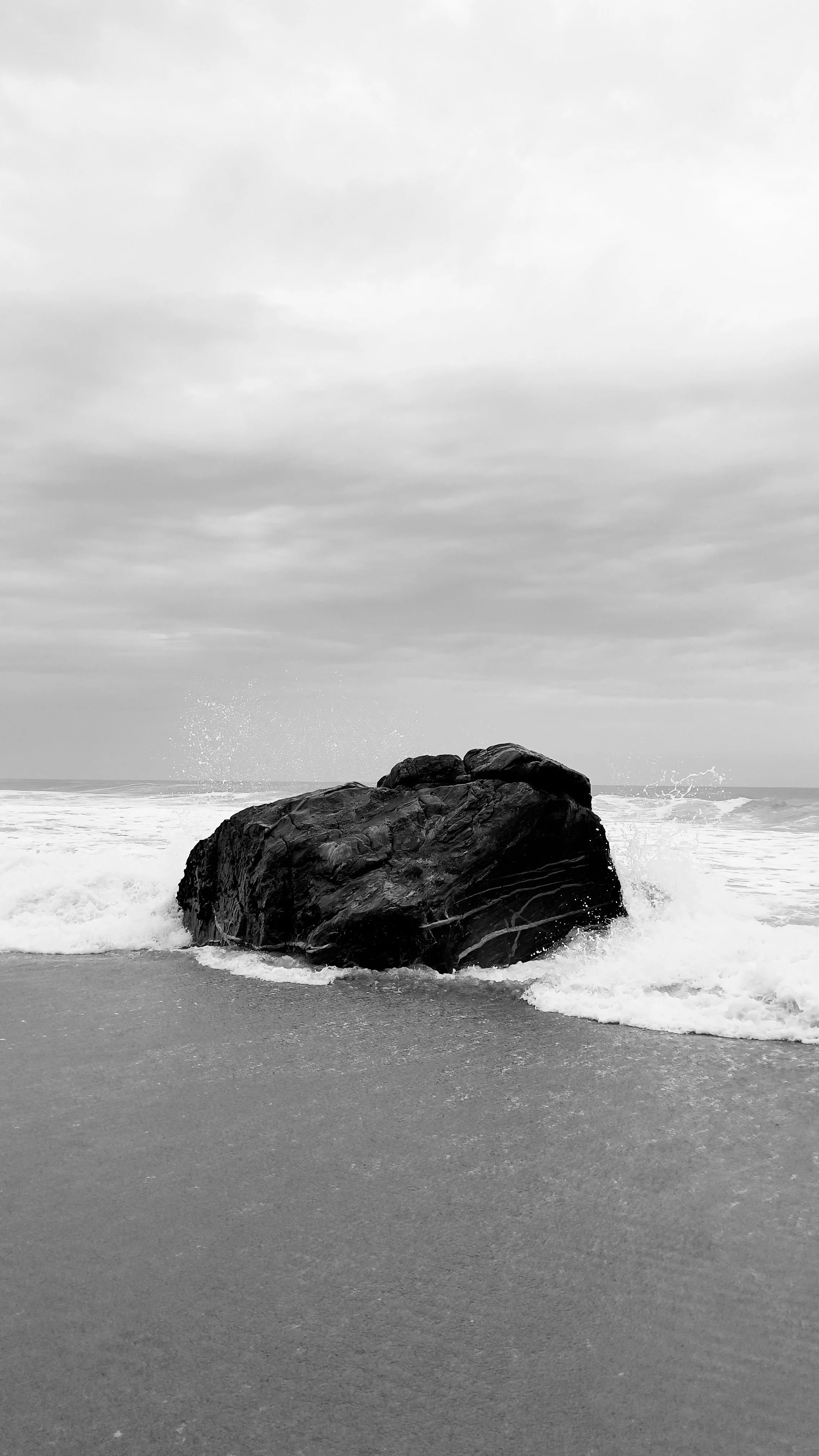 Black and white photograph of ocean waves crashing against a coastal rock, symbolizing somatic trauma grounding and resilience.