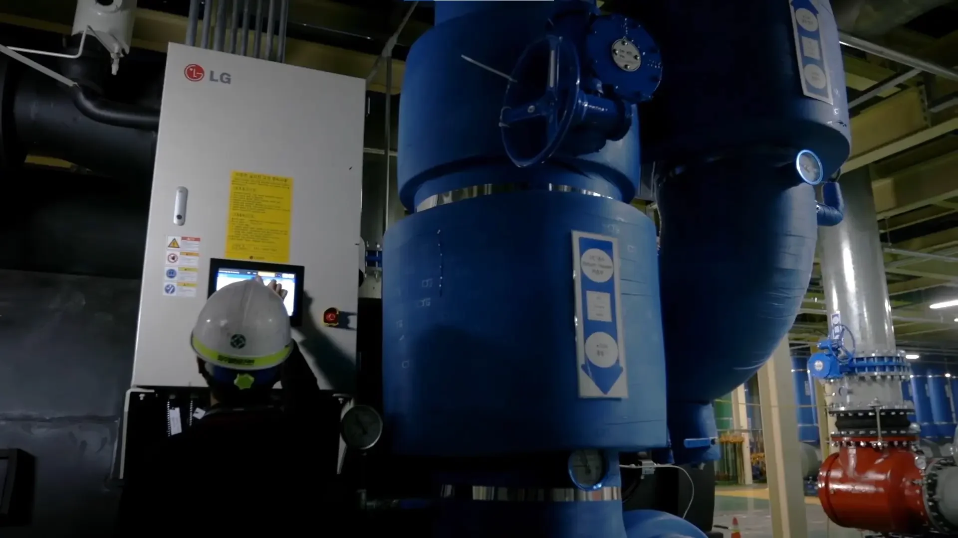 Ingeniero o técnico en casco de seguridad operando un sistema de tuberías azules en una planta industrial o de infraestructura.