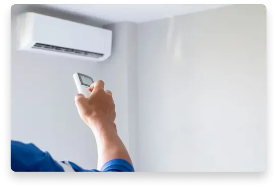 Persona encendiendo o ajustando un control remoto frente a un aire acondicionado en una pared blanca.