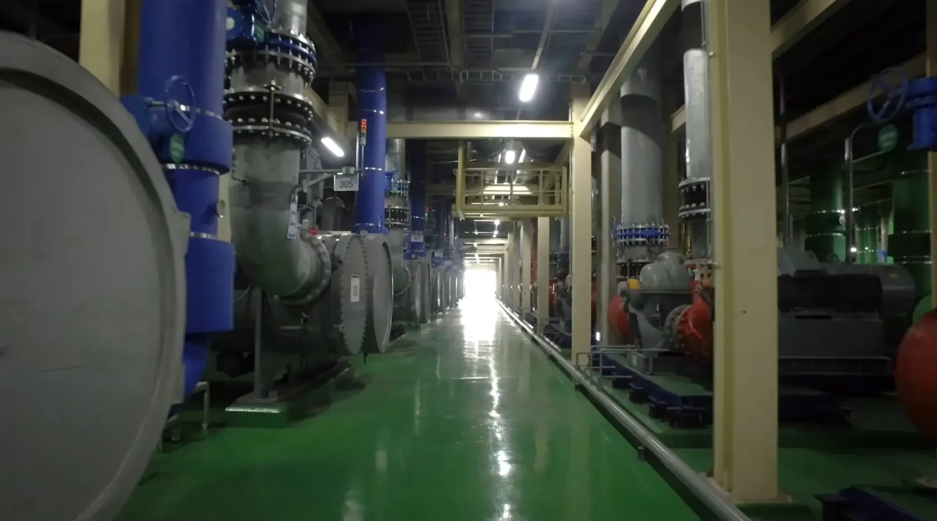 Pasillo en una planta de producción industrial con tuberías grandes, maquinaria y estructuras metálicas.