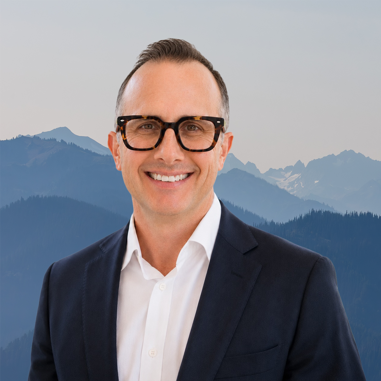 Portrait of a smiling man in a suit with mountain landscape background.