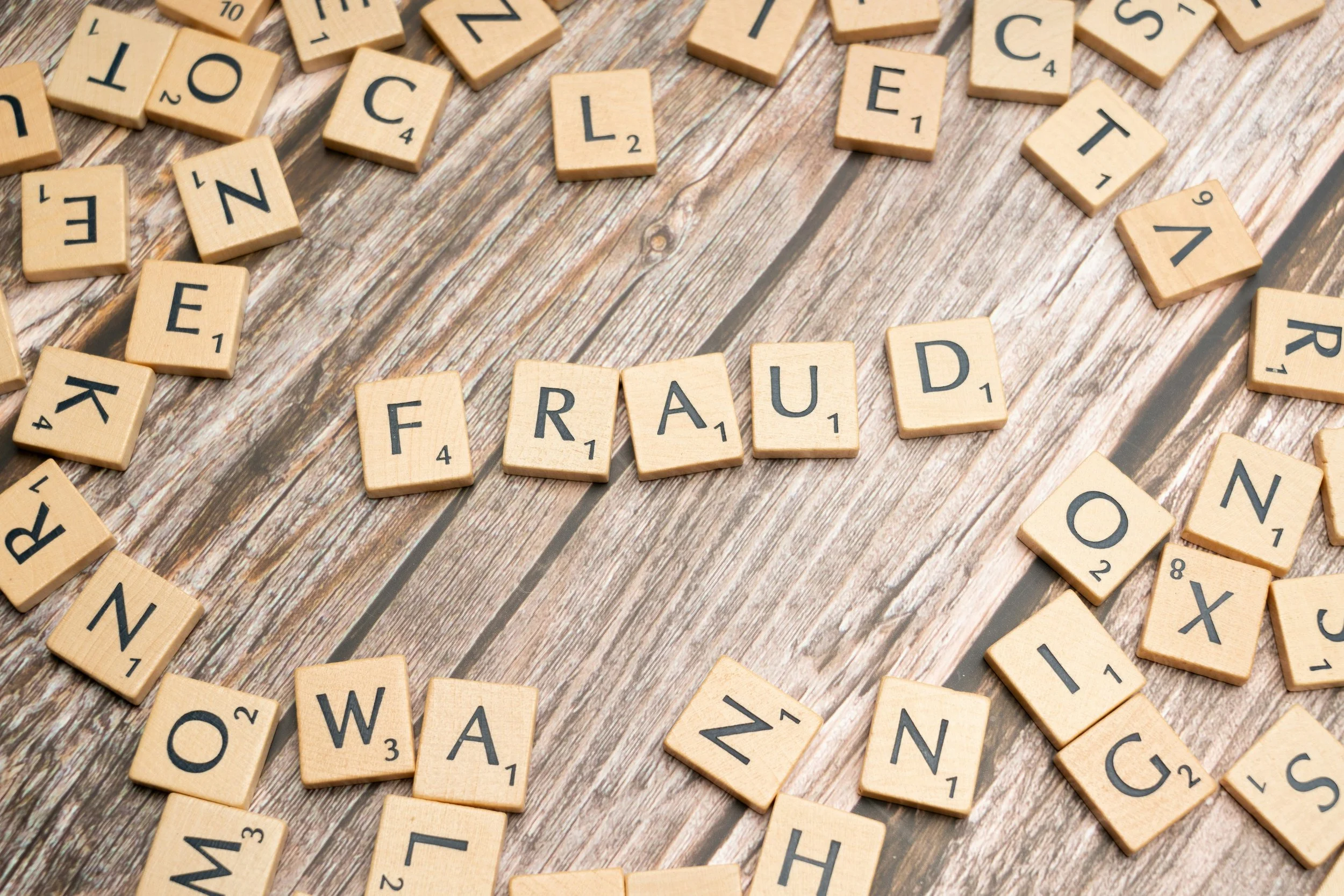 Scrabble tiles on a wooden surface spelling out 'FRAUD' with other scattered letters representing Seabrook Investigation Services, Essex based private investigators fraud and theft investigation services