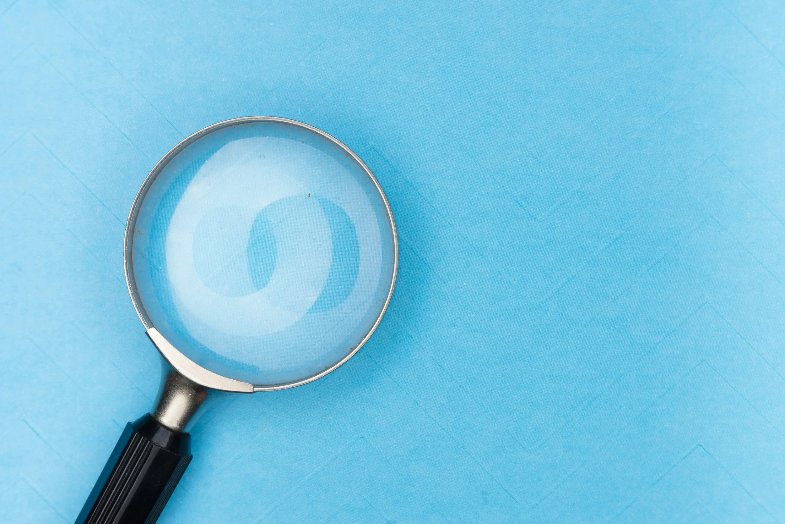 Magnifying glass with a black handle resting on a blue surface representing Seabrook Investigation Services, Essex based private investigators tracing service.