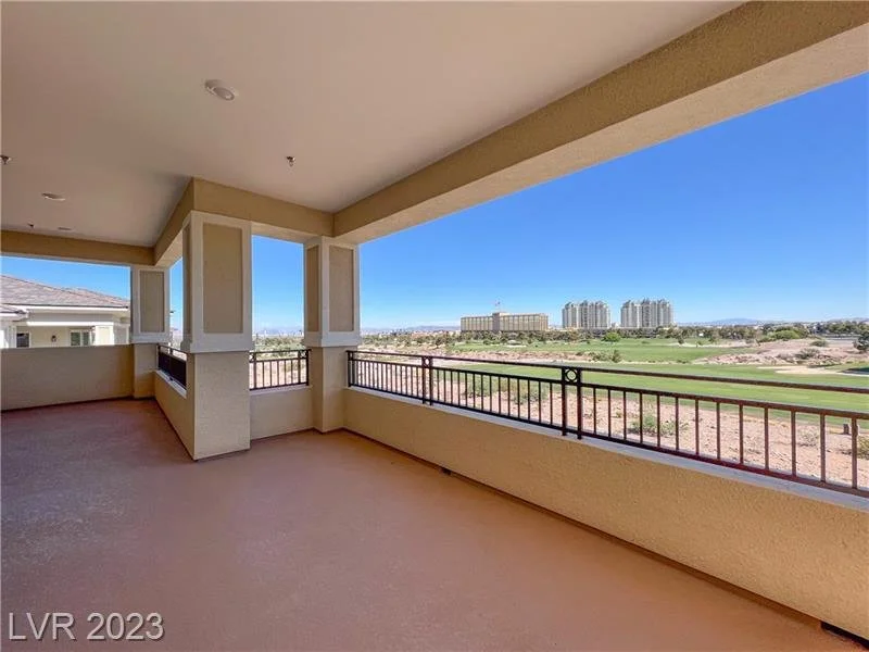 Balcony with railings overlooking a golf course, with buildings in the distance under a clear blue sky.