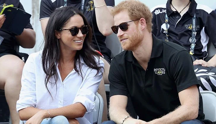 Prince Harry and Meghan Markle sitting at the Invictus Games, smiling and talking to each other.