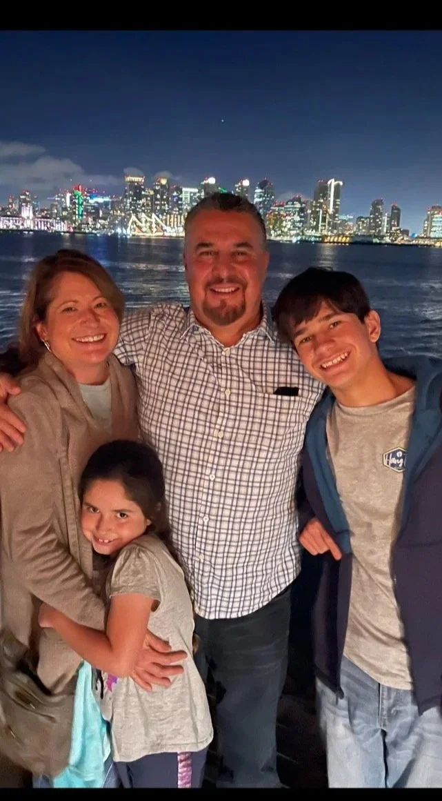 A family of five posing together at night with a city skyline and water in the background.