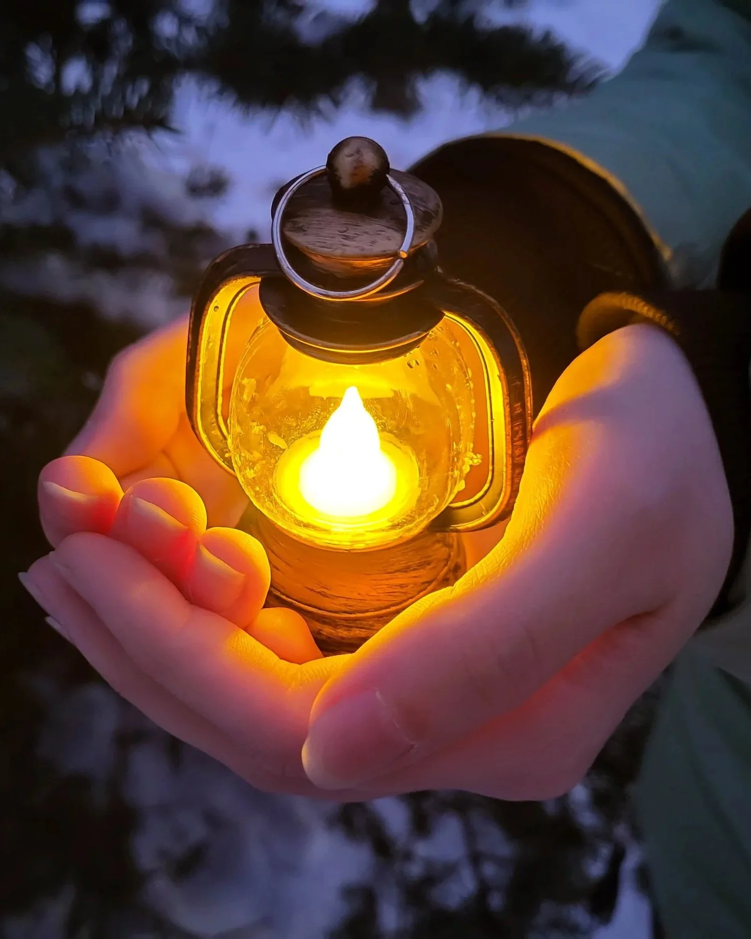 Person holding a small glowing lantern outdoors at dusk