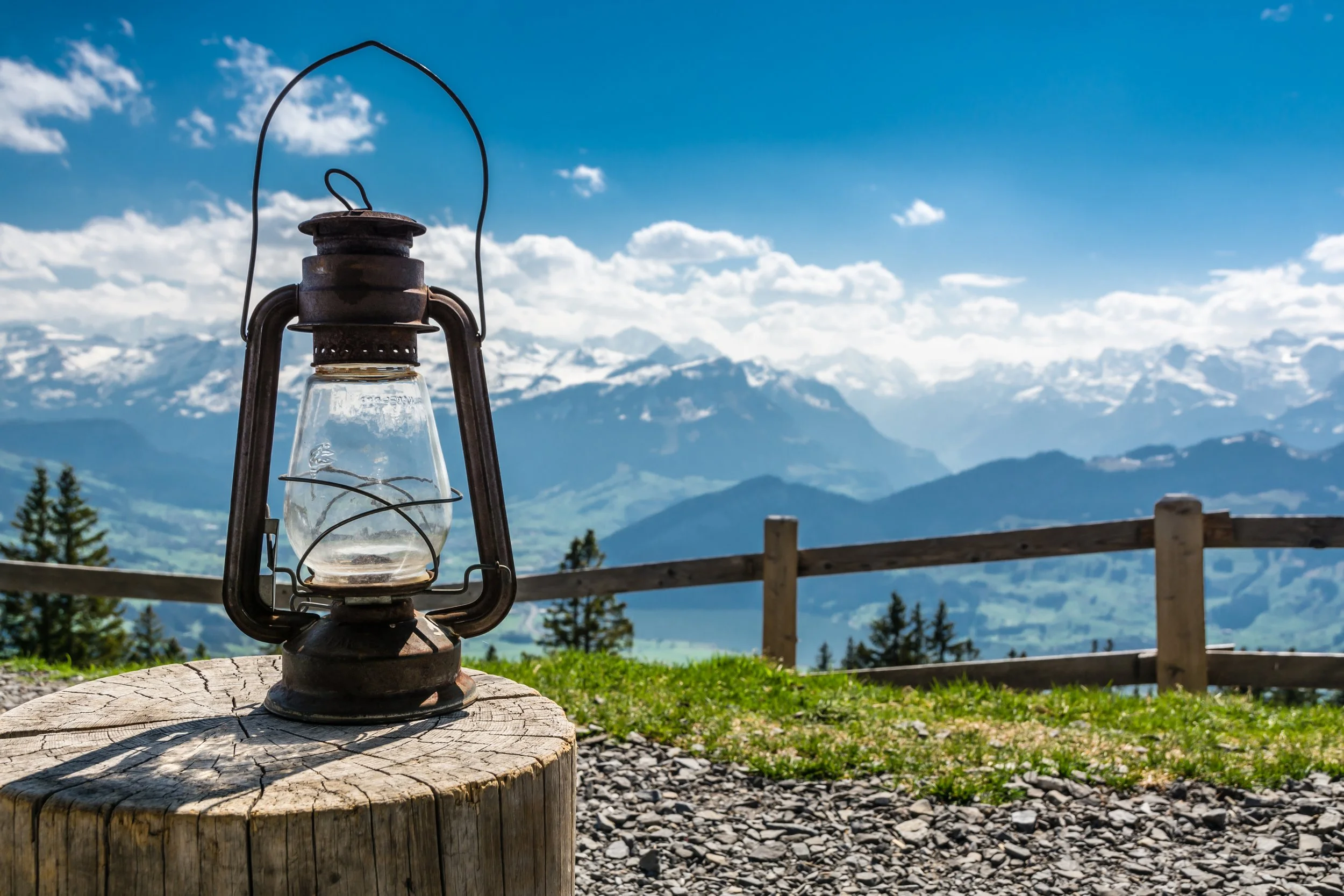 An old rusty lantern on a tree stump with mountains and blue sky in the background.