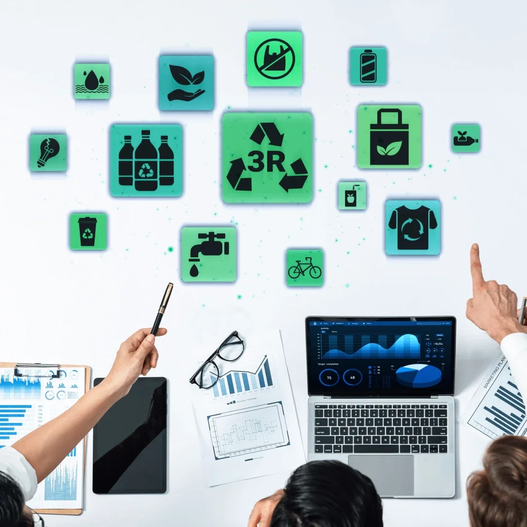 Overview of a team collaborating on environmental sustainability, with icons representing recycling, water conservation, renewable energy, waste reduction, and eco-friendly products displayed on a wall, alongside laptops, tablets, documents, and people pointing and discussing.