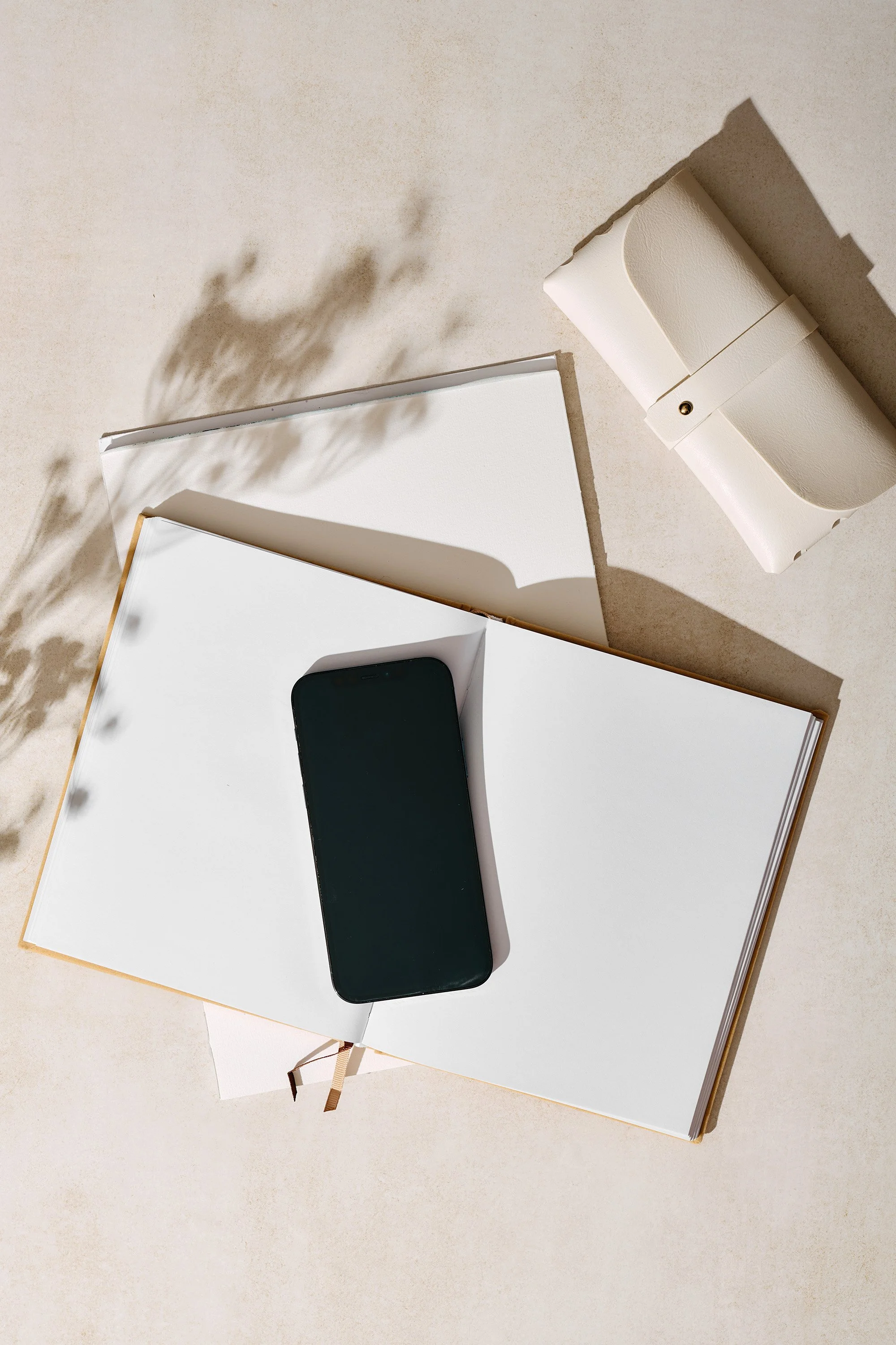 A black smartphone resting on an open white notebook or journal, with a drawer or box next to it on a white surface.