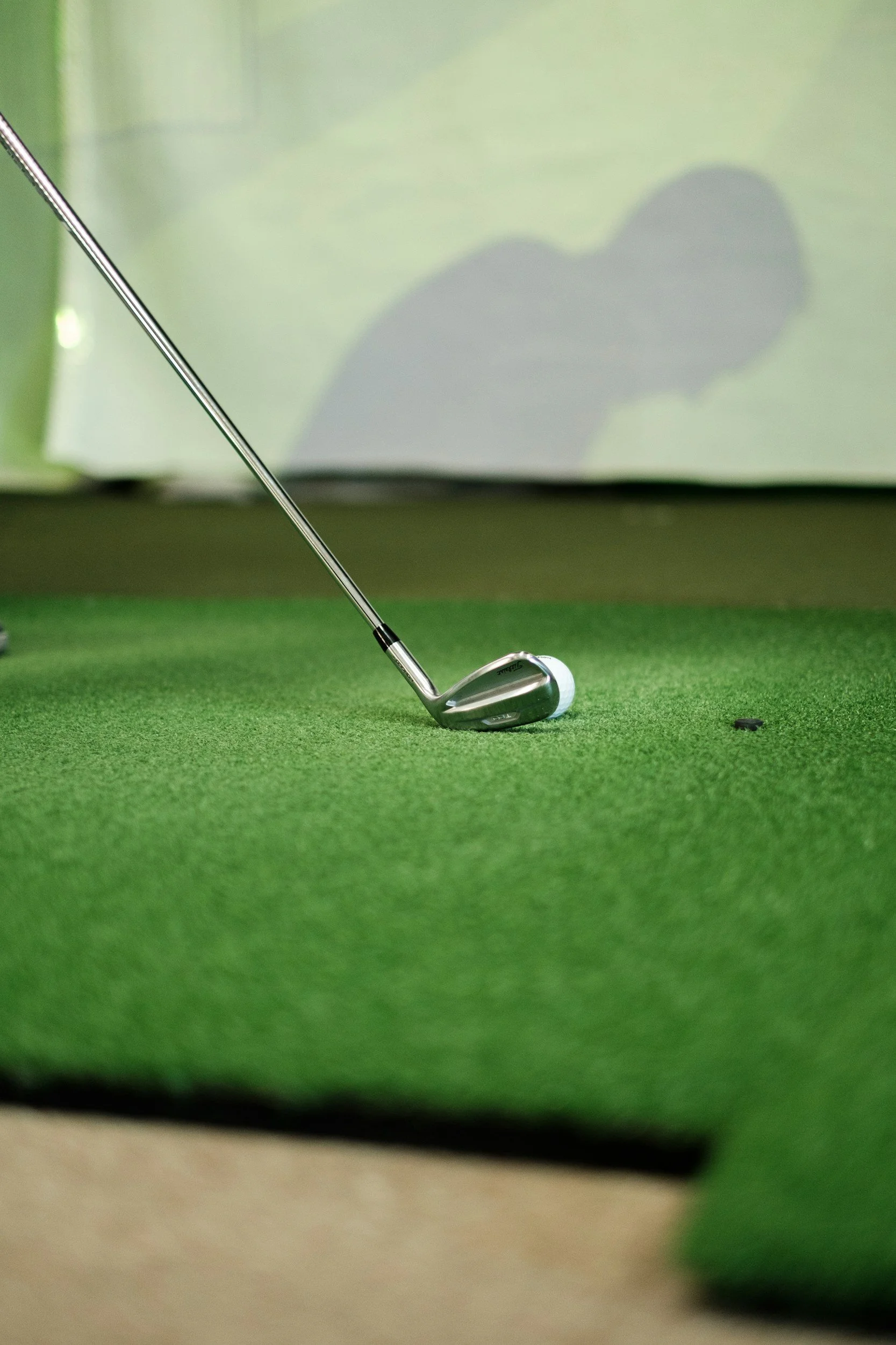 A golf club positioned on a green golf course near a golf ball.