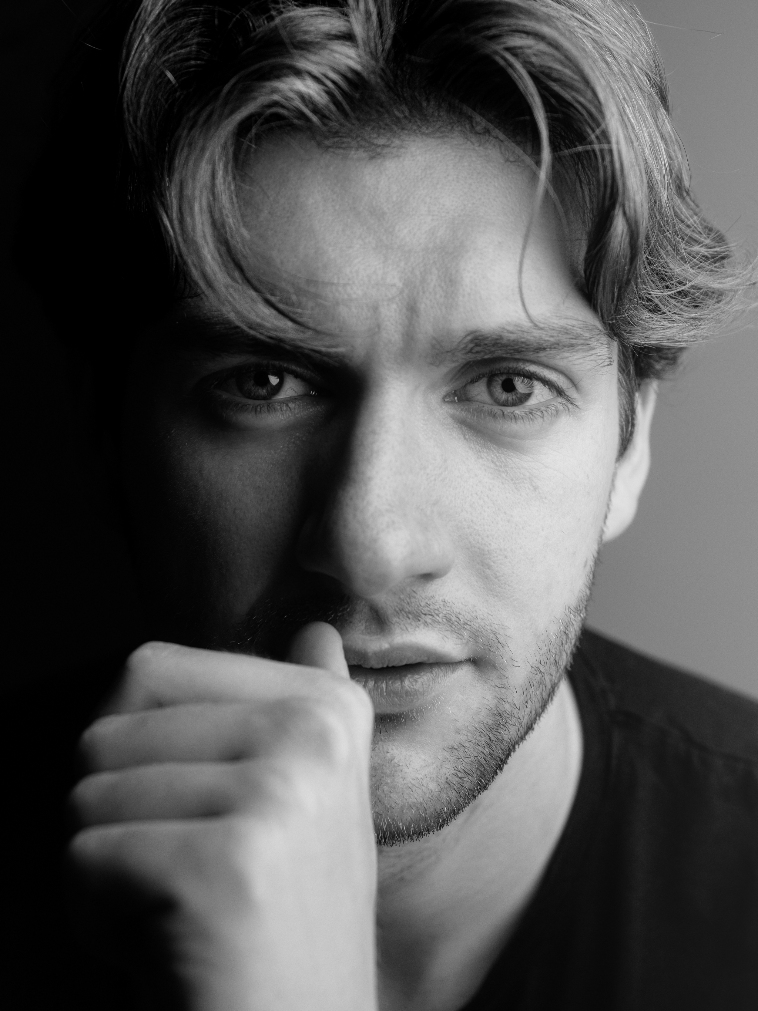 Close-up black-and-white photograph of Lyall Hardy Grey. A young man with wavy hair, looking directly at the camera, with one hand resting near his mouth.