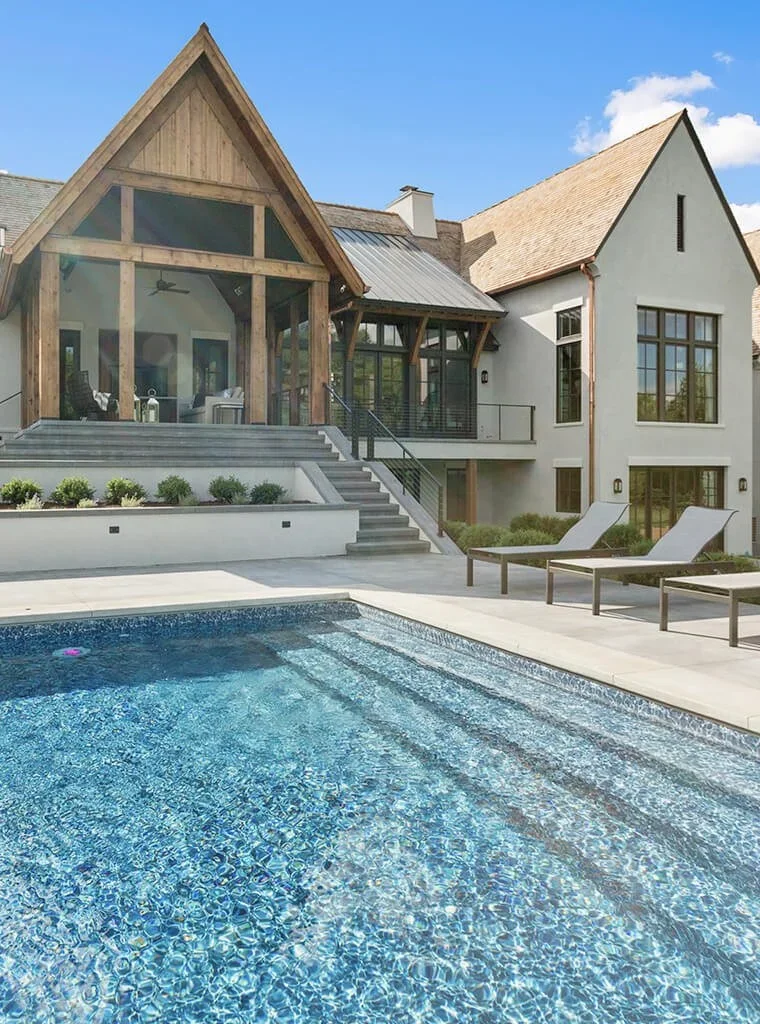 Modern house with a swimming pool in the backyard, outdoor lounge chairs, and a wooden and stucco exterior with large windows.