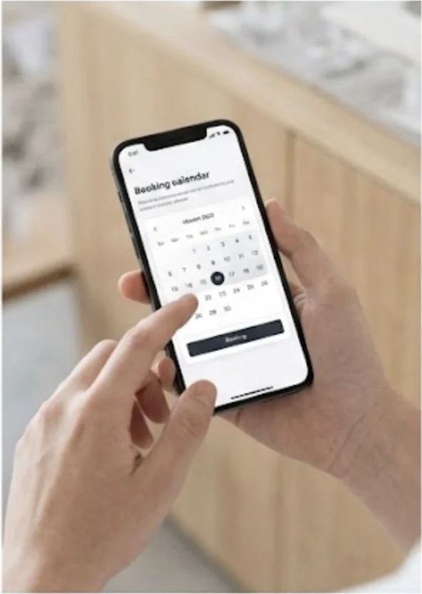 A person using a smartphone to book a reservation on a booking calendar app, displaying a calendar for December 2023.