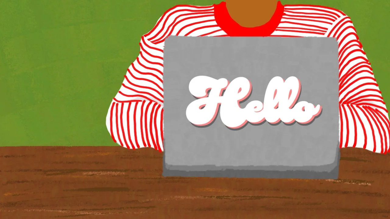 A person wearing a red and white striped shirt sitting at a wooden table, holding a laptop with the word 'Hello' on the screen, with a green wall in the background.