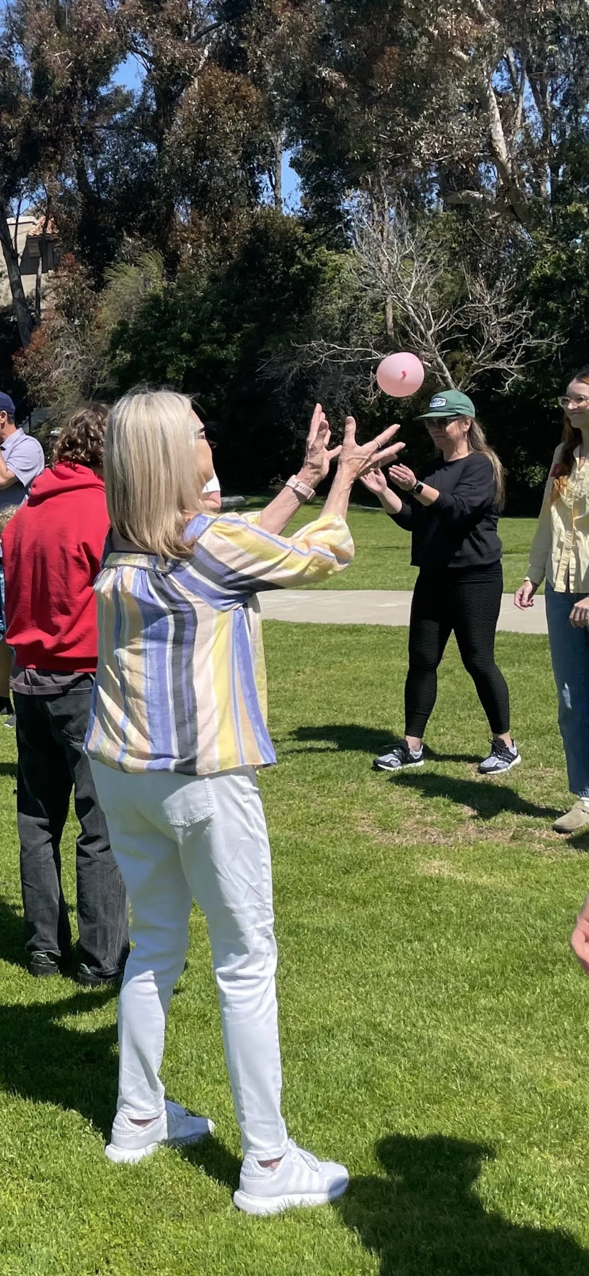 People participating in an outdoor game with a pink balloon in a park on a sunny day.