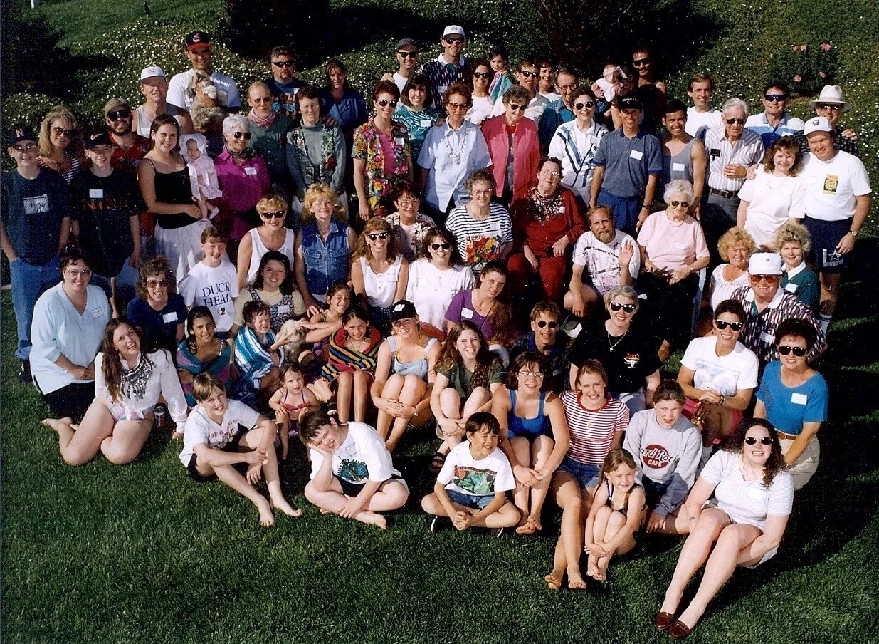 Group photo of a large diverse crowd of adults and children outdoors on a grassy area, smiling and posing for the camera.