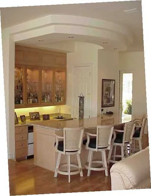 A cozy kitchen with a bar area, four bar stools, wooden cabinetry, and a built-in wine rack, with a window and a door leading outside.