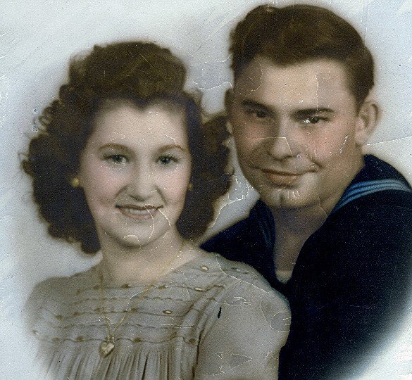 Vintage portrait of a young woman with curly hair wearing a dress and a gold necklace, alongside a young man with short hair in a sailor uniform, both smiling at the camera.