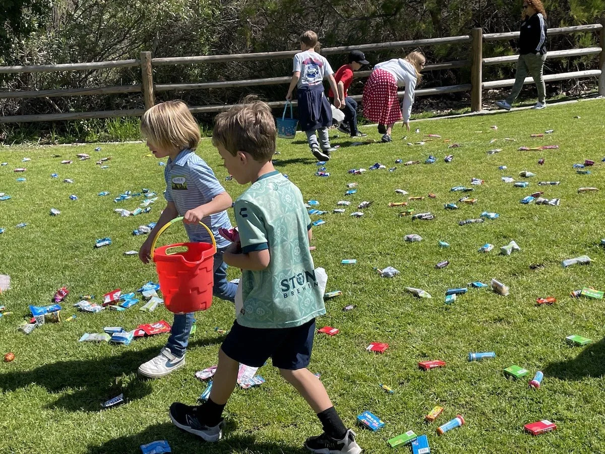 Children collecting candy scattered on the grass in an outdoor area.