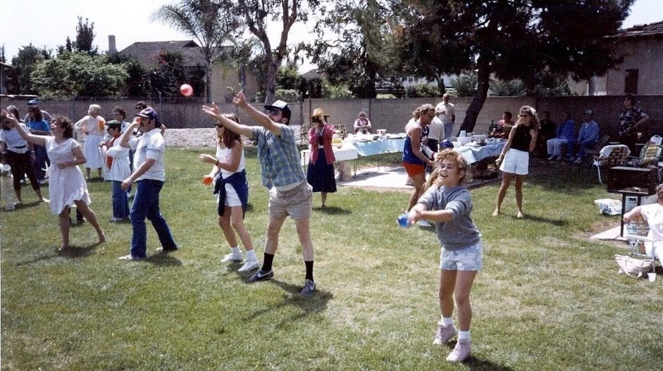 People enjoying a backyard gathering with some playing a game involving hitting a ball with a bat or stick.