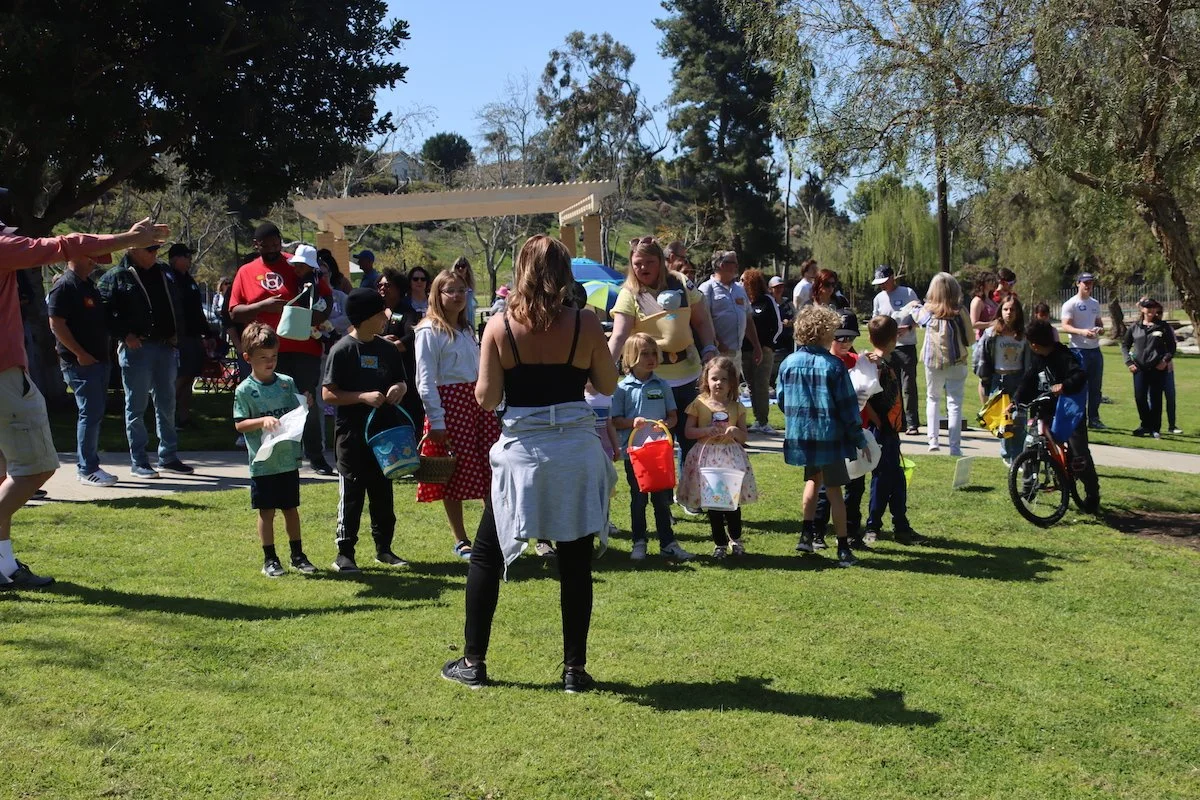 Group of children and adults standing on grass in a park, participating in an outdoor event on a sunny day.