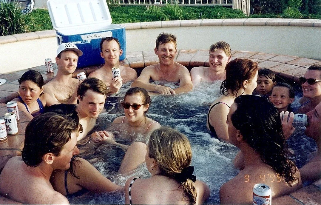 Group of people enjoying a hot tub party outdoors on a sunny day, holding cans of Miller Lite beer, with some people smiling and chatting.