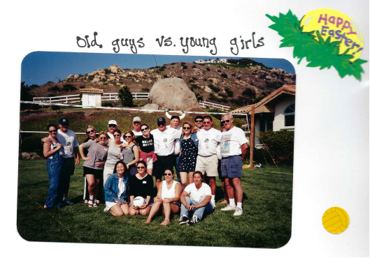 A group of old men and young women posing outdoors on grass with hills, rocks, a fence, and houses in the background. Text above reads 'Old guys vs. young girls'. A green leaf graphic with yellow text says 'Happy Easter' in the top right corner.